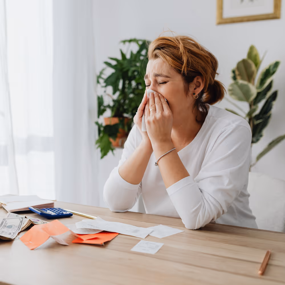 Woman sitting at a table crying into a tissue with bills, cash, and calculator on the table.