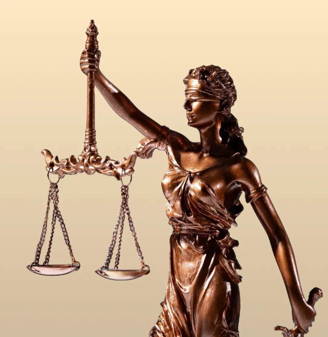 Blindfolded Lady Justice bronze statue holding balanced scales against a beige background.