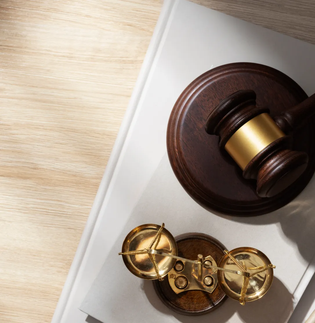 Wooden judge gavel and brass balance scale on a white book on a light wooden surface.